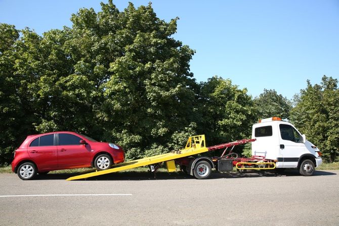 Red SUV loaded on a tow truck beside a tree-lined road