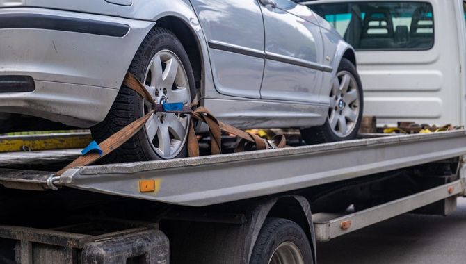 Silver car strapped to a flatbed tow truck with blue tie-down straps