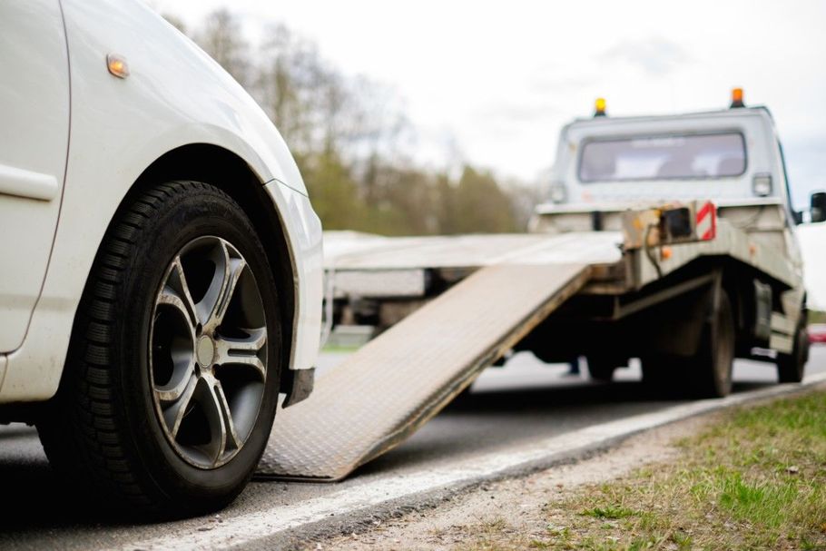 White car loaded on a tow truck with a ramp on a roadside