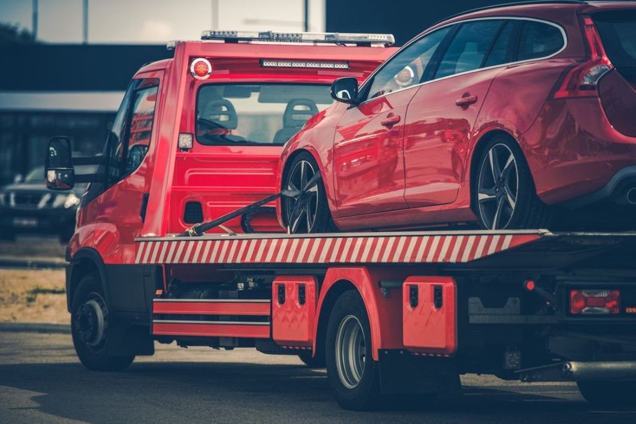 Red hatchback on a tow truck flatbed, with another truck in the background